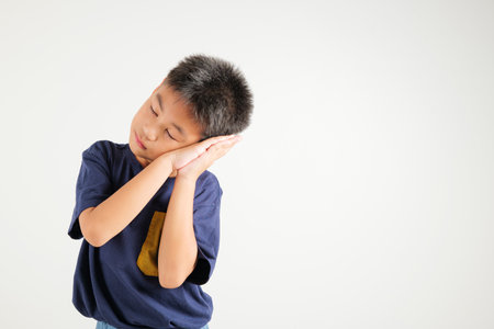 Portrait Asian young kid boy pretended emotions sleeping tired eyes closed dreaming with hands together near face, studio shot on white background, with copy space, insomnia concept, primary childの写真素材