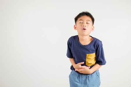 Portrait of Asian young kid boy has stomachache, primary child abdominal pain suffering from stomach ache, studio shot isolated on white background, food poisoning, Health and medical gastritisの写真素材