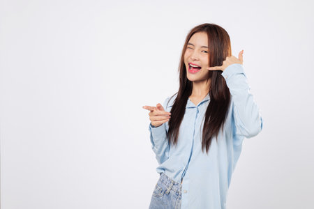 Making a call me sign, one woman uses fingers like telephone and pointing finger, second woman smiles and poses with hand up near ear, isolated on white background.の写真素材