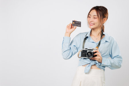 Travel lover with credit card bank and photo camera plans next travel. Cheerful Traveler tourist woman excited for vacation, holding her retro camera and payment card. isolated studio white backgroundの写真素材