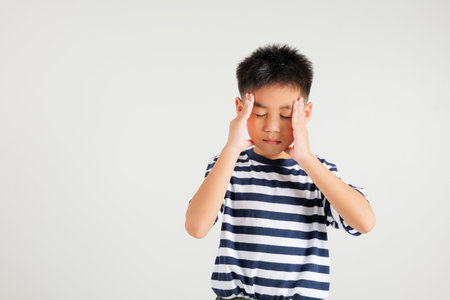 Portrait of Asian young kid boy sad tired strain face holding hold head by hands, stress primary child person unhappy closed eyes problem headache, studio shot isolated on white backgroundの写真素材