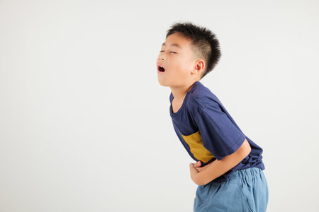 Portrait of Asian young kid boy has stomachache, primary child abdominal pain suffering from stomach ache, studio shot isolated on white background, food poisoning, Health and medical gastritisの写真素材