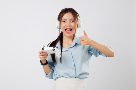 Game excitement on excited Asian young woman face as she enjoys the video game while smiling, wearing headphones and giving a thumb up gesture with fingers. isolated studio white backgroundの写真素材