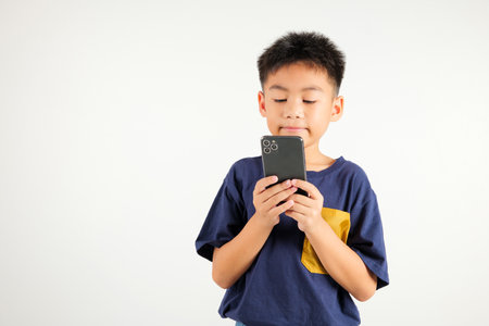 Happy Asian portrait cute young kid boy smiling excited using smart mobile phone studio shot isolated on white background, Thai child surprised holding reading message gesture on smartphoneの写真素材