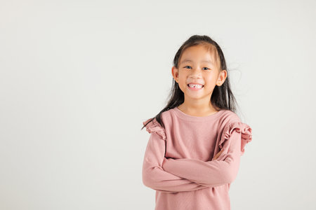 Asian happy portrait cute young kid girl smiling confidence with arms crossed studio shot isolated on white background and copy space, kindergarten children person lifestyle arm foldedの写真素材