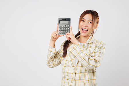 Young Asian accountant woman shows a calculator with blank screen and holds another calculator in her hand, symbolizing financial success and smart tax saving. isolated studio white backgroundの写真素材