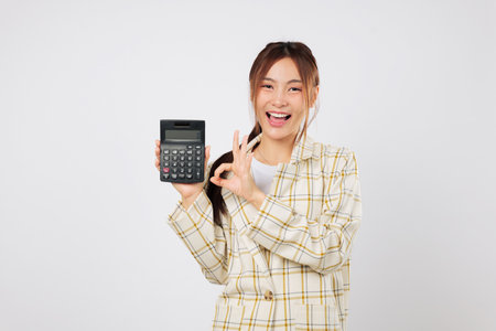 Smiling woman holding calculator and making OK gesture, showing calculator again as a sign of approval and financial success in business and marketing. isolated studio white backgroundの写真素材