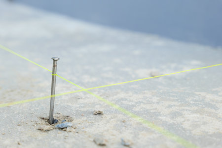 A close-up of a nail driven into rough concrete with intersecting yellow lines, representing...