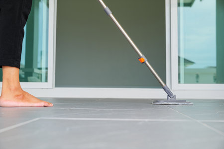 Woman mops the indoor floor, cleaning the front area of her home with a mop and rag. Housewife dedicated to maintaining cleanliness. Represents professional housekeeping and house maintenance conceptsの写真素材