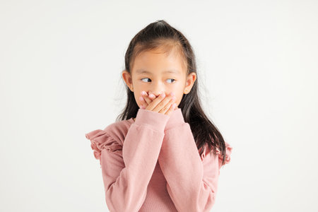 Asian portrait young kid girl standing surprised excited shocked covering mouth with hands for mistake on white background, kindergarten child secret concept with copy space for textの写真素材