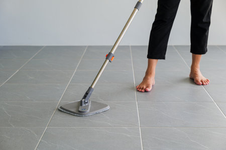 Woman mops the indoor floor, cleaning the front area of her home with a mop and rag. Housewife dedicated to maintaining cleanliness. Represents professional housekeeping and house maintenance conceptsの写真素材