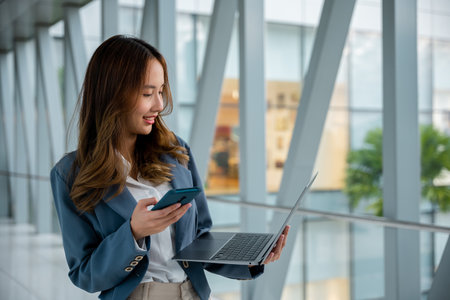 Modern businesswoman on-the-go, using laptop and cell phone to stay connected and productive while in airport.の写真素材