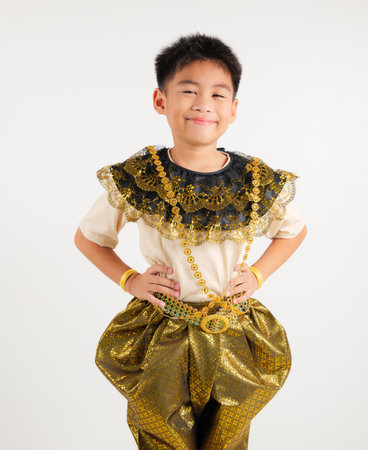 Portrait of Thailand kid boy smiling traditional Thai dress costume stand akimbo gesture in studio shot isolated white background, Happy primary child standing on waist supportの写真素材