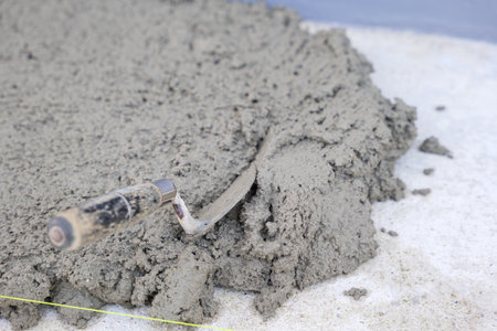 Construction scene featuring a gray concrete surface, a trowel, pull tabs, and wedges used for tile leveling, essential for precision and quality.の写真素材