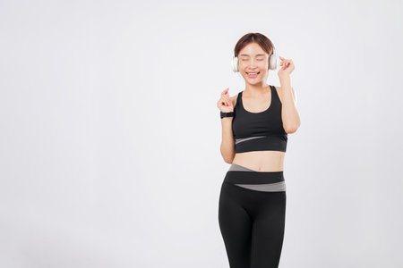 Dance is her favorite part of every workout session in sporty headphones. As the beat drops, she cannot help but dance again, glowing with music and fitness energy. isolated studio white backgroundの写真素材