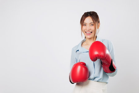 Boxing energy and business strength shown by a smiling Asian young woman. Ready in guard pose, combining fitness and strong lifestyle through red boxing glove. isolated studio white backgroundの写真素材