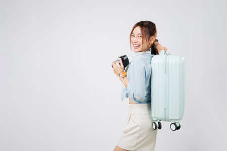 Travel dreams and travel spirit in happy young Asian woman with photo camera. Tourist ready with luggage and suitcase, smiling for her vacation trip. isolated studio white backgroundの写真素材
