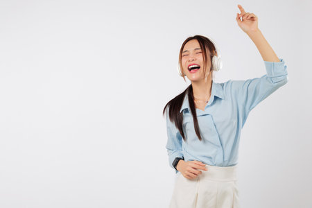 Happy young Asian woman dancing and listening music with headphones and raised hands while enjoying lifestyle full of smile, joy, People emotions, and music. isolated studio white backgroundの写真素材