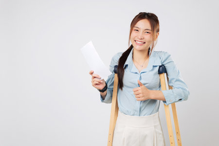 Broken leg or foot woman with crutches holds bill payment paper, recovering from accident and leaning on crutches during her healing journey. isolated studio white backgroundの写真素材