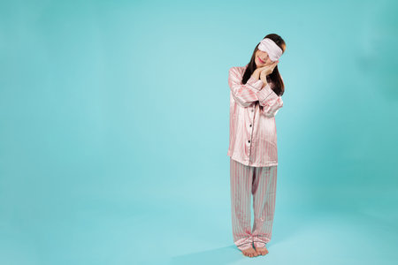 Dreamy Asian woman wearing sleep mask, cover eye, rests hands mimicking sleep, young girl in...