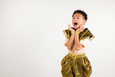 Portrait Thailand kid boy smiling traditional Thai dress costume raises his fists in celebration of his success, studio isolated white background, primary child saying yes with excitement winningの写真素材