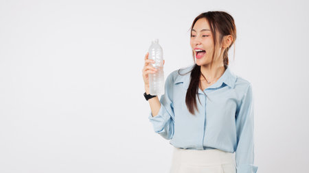 Happy asian woman hold plastic water bottle hydrated after a workout, she enjoys to drink a cool fresh drink for healthy lifestyle benefits and positive smile, isolated studio white backgroundの写真素材