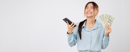 Happy Asian woman showing phone and holding money fan, online shopping winner excited about finance,...