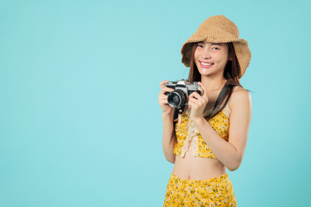 Happy young asian tourist woman camera in hand, smiling during her summer vacation, excited for travel, holding a vintage camera while on travel, headshots isolated studio blue backgroundの写真素材