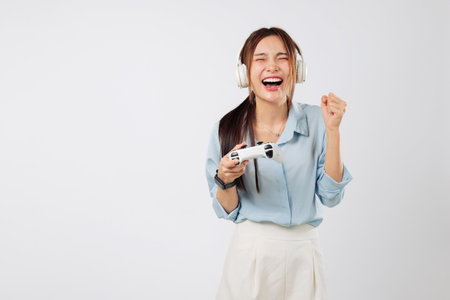 Game action captured as teen woman raises fist in victory, headphones on, eyes on screen, gripping game controller while smiling proudly. isolated studio white backgroundの写真素材