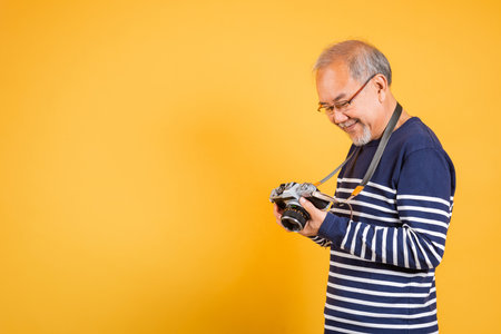 Portrait of an old man wearing glasses, looking at a picture on the screen of a vintage SLR camera,...