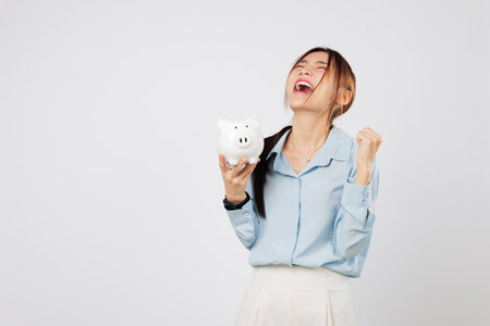 Excited woman happy with a fist up to save money holding piggy bank and piggy win symbol, showing success in finance and smart investment journey. isolated studio white backgroundの写真素材