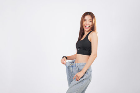 Oversized jeans make her slim waist even more noticeable and impressive. Holding up another oversized pair, she beams with happiness and pride. isolated studio white backgroundの写真素材