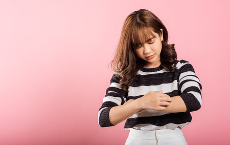 Asian woman itching her scratching her itchy arm on pink background with copy space, Medical and...