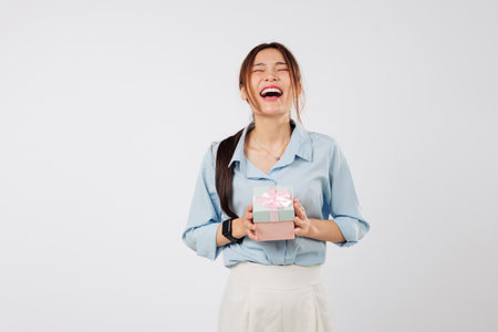 Gift wrapped beautifully in pink ribbon is held by excited woman, expressing joy and smile while posing with the gift box on her birthday. Portrait isolated studio white backgroundの写真素材