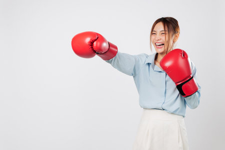 Boxing strength shines as an Asian young woman throws a powerful punch. Her fit look and strong posture reflect the mindset of a true kickboxer. Isolated studio white background.の写真素材