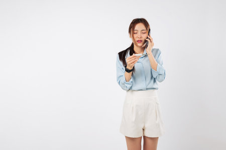 Woman sick, disease setting in, talking on her phone and checking temperature with thermometer, she looks worried she may be sick, calling doctor to explain her flu symptoms, isolated white backgroundの写真素材