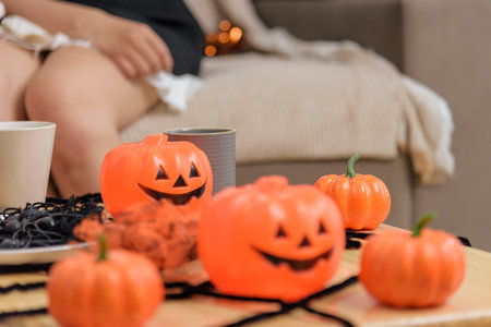 Halloween decorations are set out on a table in front of a person relaxing, featuring orange pumpkin figures, black spiderwebs, a tan mug, and soft lighting to create a festive scene.の写真素材