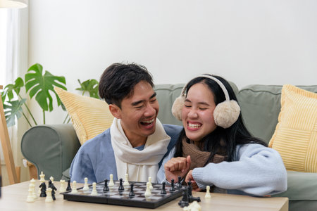 Winter brings happy couple, people enjoying indoor day at home, laughing playing chess, wearing cozy warm clothes for comfort during cold winter season, sharing leisure time.の写真素材