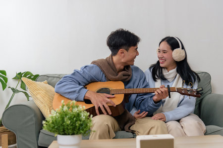 Winter couple, happy people enjoy family home indoor activity, man playing guitar for woman, cozy warm atmosphere during cold winter season, smiling.の写真素材