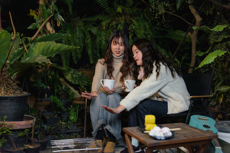 Winter night friends camp outdoor forest, two joyful women enjoy warm drinks, sharing stories,...
