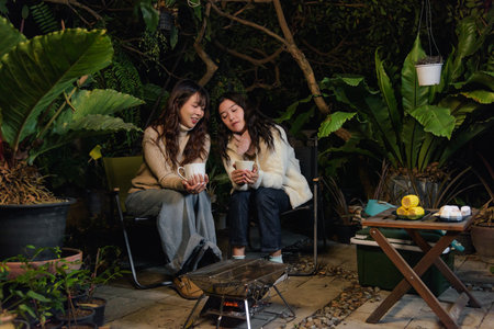 Winter outdoor gathering for happy women friends, people in garden enjoying warm drinks by glowing...