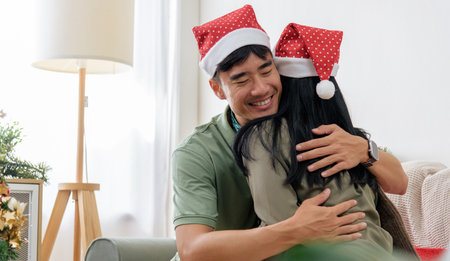 Christmas loving couple share happy holiday embrace, winter joy fills cozy home, wearing festive santa hats with smiles during special christmas season.の写真素材
