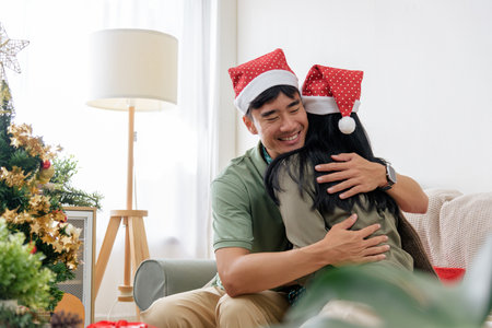 Christmas day brings happy couple love, embracing winter holiday joy at home, wearing Santa hats, sharing warm intimate loving moments near festive christmas tree decorations.の写真素材