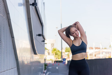 Fit woman performing sport exercise workout outdoor stretches arms, preparing for active day, displaying strong physique, feeling refreshed, achieving fit lifestyle goals confidently.の写真素材