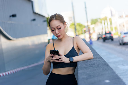 Workout woman, sport exercise enthusiast, checks mobile phone outdoor, pausing active fitness regimen. Healthy lifestyle individual completes urban workout, resting among people.の写真素材