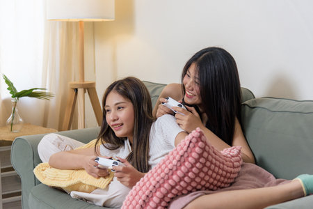Two young women friends play video game at home, teenagers enjoying fun pastime with controllers,...