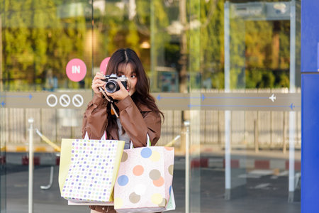 Shopping woman enjoys lifestyle fashion holds bags from black friday mall sales, people watch her posing with camera outside shop capturing fun holiday moments.の写真素材