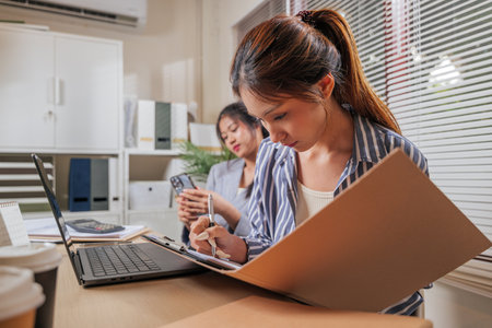 Business women work from home office, young people collaborate, team learning online, one woman concentrates writing, another colleague uses phone communication.の写真素材