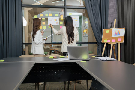 Business women meet, busy team people work on project in important meeting, discussing business strategy in modern conference room, collaborating, analyzing charts and data on glass wall.の写真素材