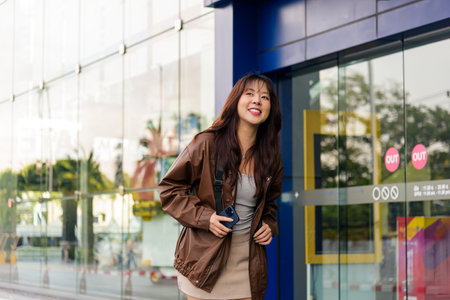 Asian woman enjoying shopping lifestyle, holding shopping bags near modern mall, happy fashion shopper posing outdoor for retail black friday deals, city street.の写真素材
